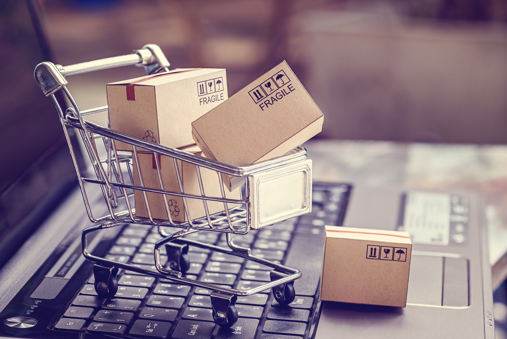 Image of a laptop and a miniature shopping cart brimming with packages, symbolizing comprehensive Ecommerce Solutions.